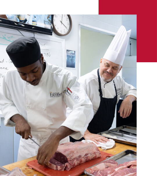 an escoffier culinary arts instructor watches a culinary student cut ribeye steaks